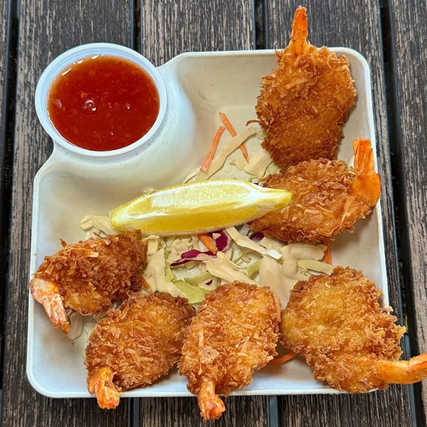 Six crispy coconut shrimp with a side of sweet chili sauce, lemon, and shredded cabbage.