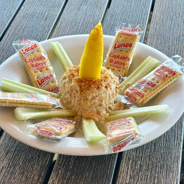 A white plate with a mound of crab dip, celery sticks, and individually wrapped crackers.