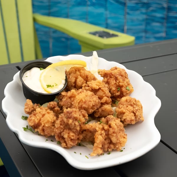 Fried popcorn shrimp with a side of tartar sauce and lemon, on a table by a pool.