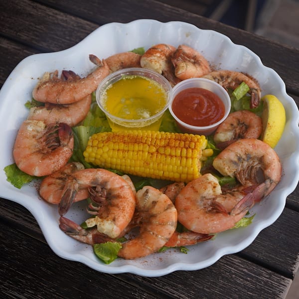 A white platter of seasoned shrimp, corn on the cob, melted butter, ketchup, and lemon.