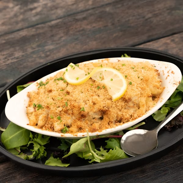Baked mac and cheese with breadcrumbs, parsley, and lemon slices, served on a bed of greens.