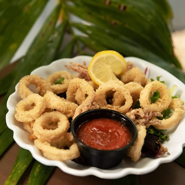 Crispy fried calamari rings with a side of marinara sauce and a lemon wedge on a white plate.