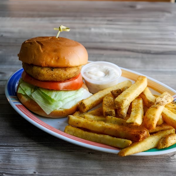 A crispy chicken sandwich with lettuce and tomato, served with seasoned fries and dipping sauce.
